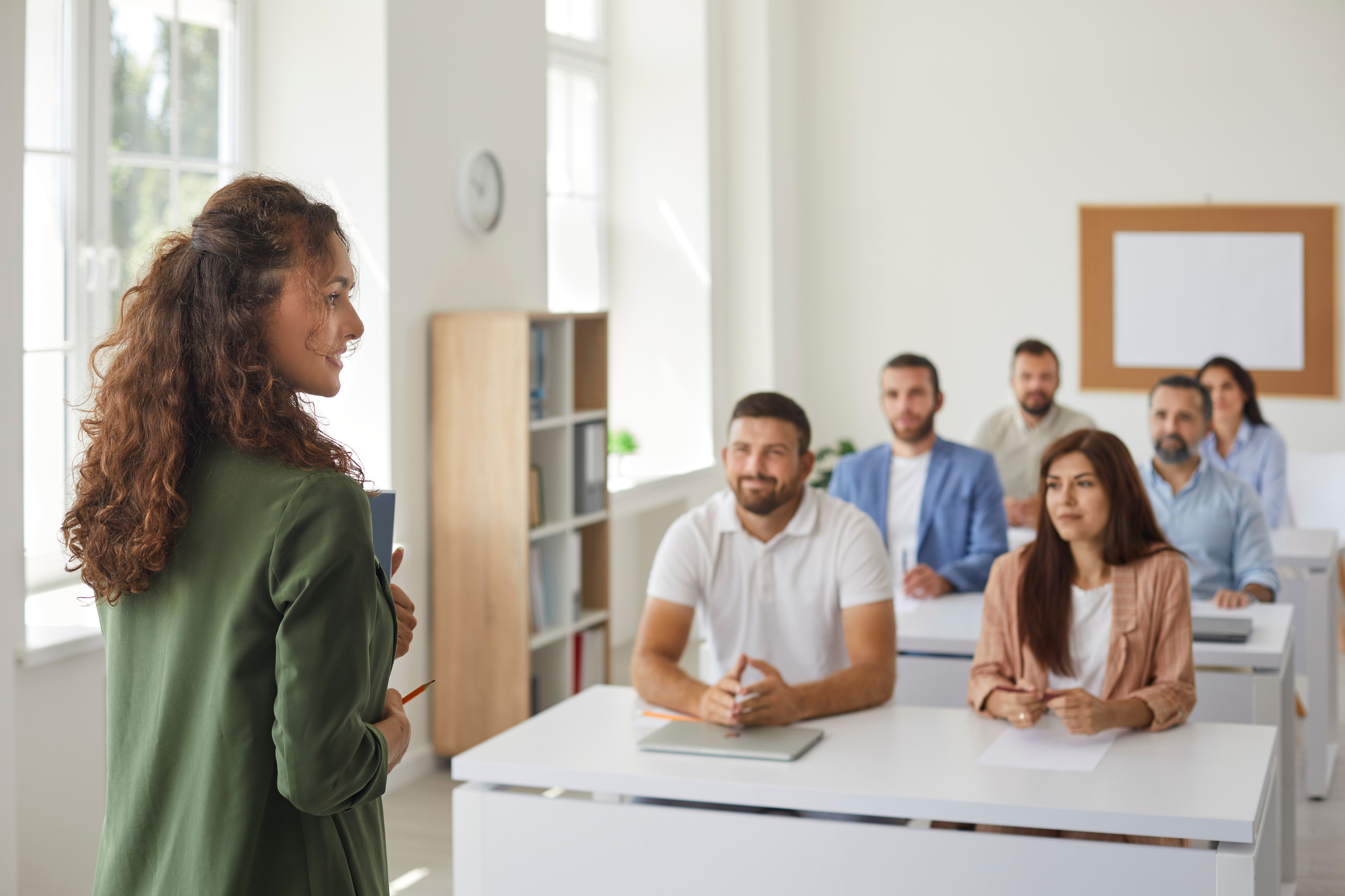 Business Teacher Standing against Blurred Classroom Background with Her Adult Students